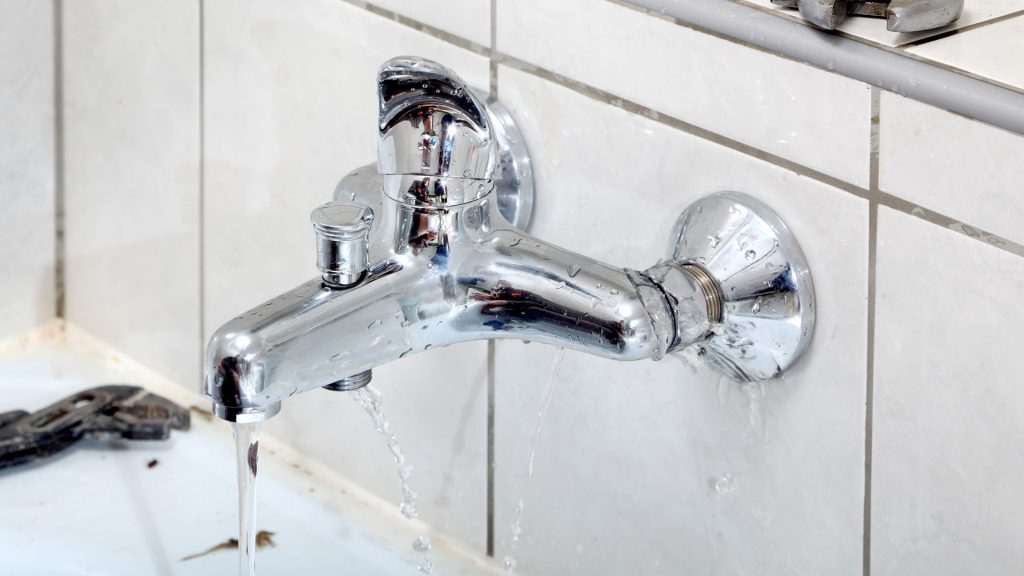 Dripping chrome faucet with water flowing, illustrating plumbing maintenance issues and potential repairs.