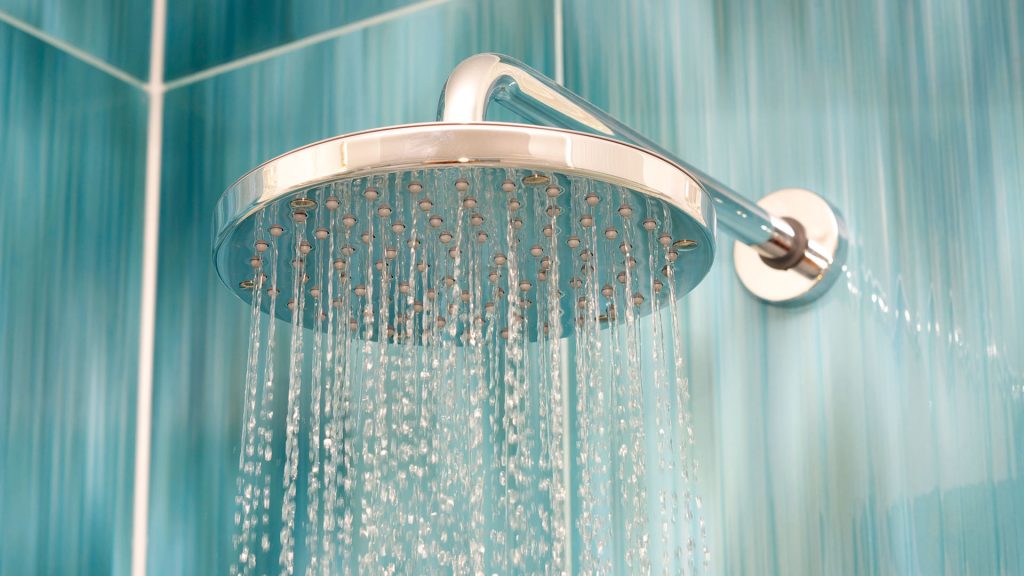 Modern showerhead with flowing water against a blue tiled background, illustrating plumbing fixtures and maintenance solutions.